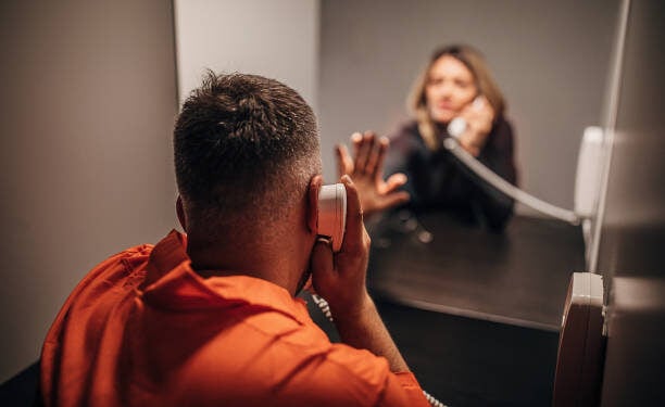 Sad young woman and her husband sitting in prison visiting room.