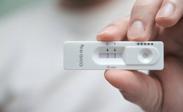 Close-up of a hand holding a positive antigen test for COVID-19. SARS-CoV-2 antigen rapid test kit.