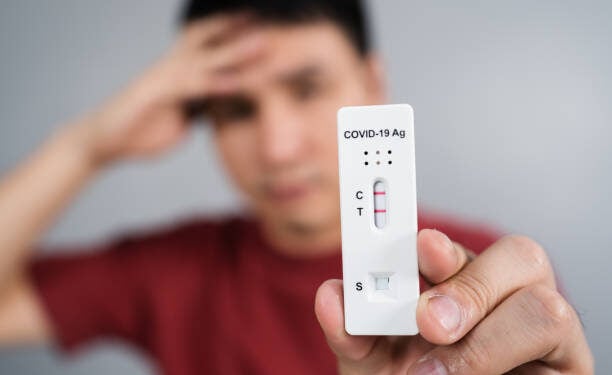 young stressed man holding Coronavirus(Covid-19) positive test result with Antigen Rapid Test kit (ATK)