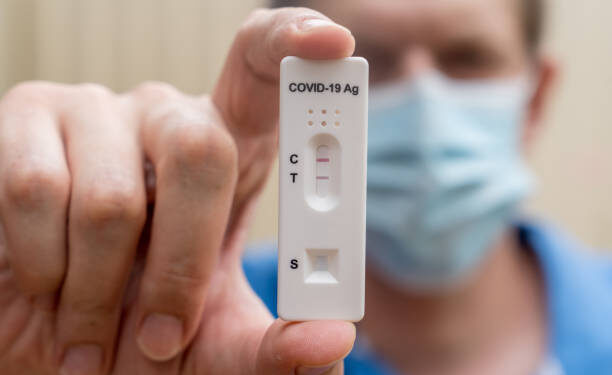 Man wearing face mask holding Covid-19 rapid antigen test cassette with negative result of rapid diagnostic test. Self-testing kit at home