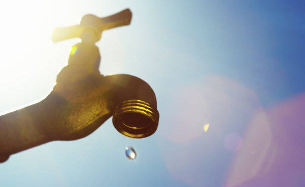A single droplet falls from a faucet, symbolizing water scarcity or drought.