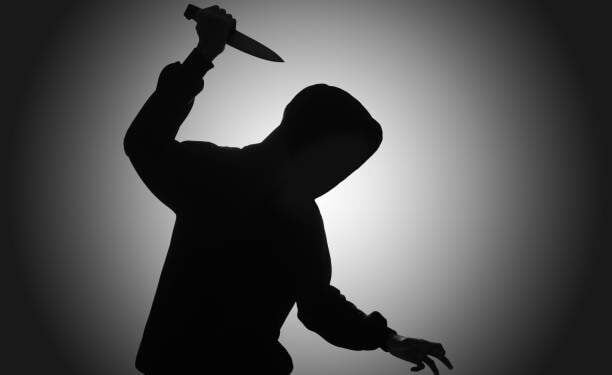 Mysterious man wearing black hoodie holding a knife to stab someone. Crimes and criminality concept