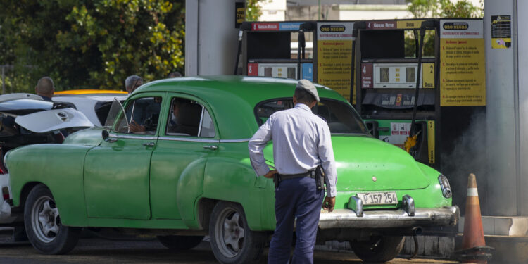 Un policía (de espaldas) observa a un coche antiguo en una gasolinera, hoy en La Habana (Cuba). EFE/Yander Zamora