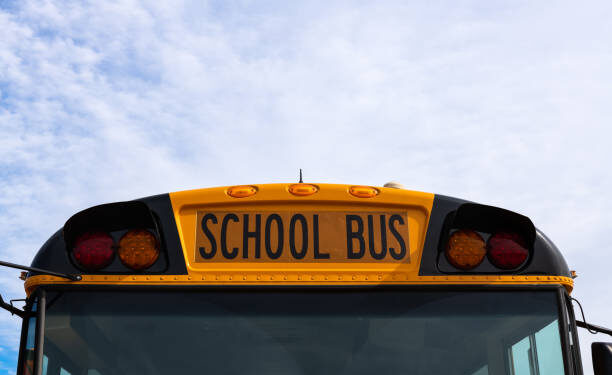 Close-up view of a yellow school bus sign and lights with blue sky background.