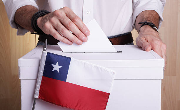 A man inserting a ballot to a ballot box.  Chilean flag in front of it.