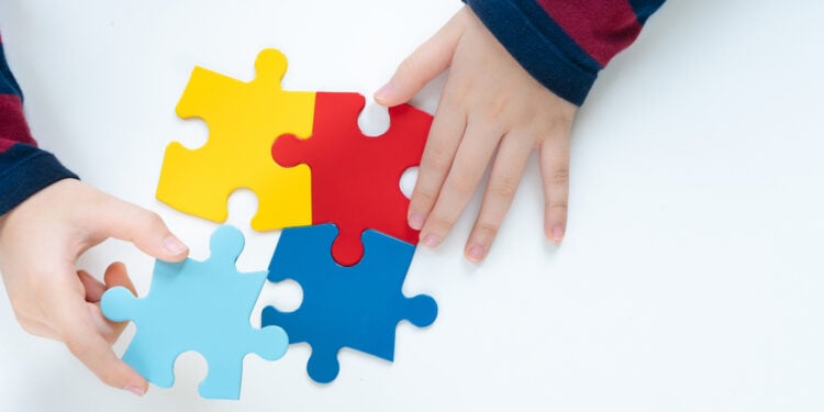 Top view hands of a little child arranging color puzzle symbol of public awareness for autism spectrum disorder. World Autism Awareness Day, Caring, Speak out, Campaign, Togetherness. Isolated.