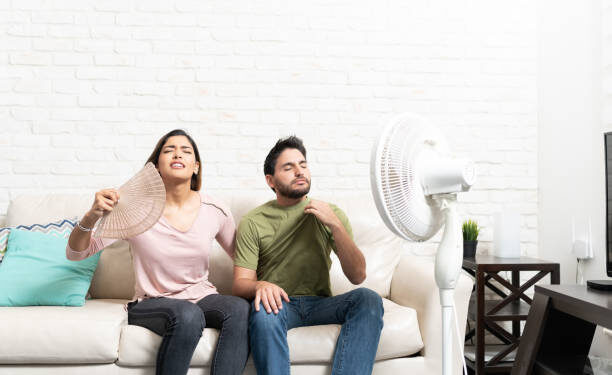 Latin heterosexual couple feeling hot while sitting in front of fan at home