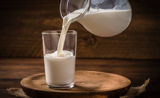 Front view of a pitcher pouring milk into a drinking glass on a rustic wooden background. Low key DSLR photo taken with Canon EOS 6D Mark II and Canon EF 24-105 mm f/4L