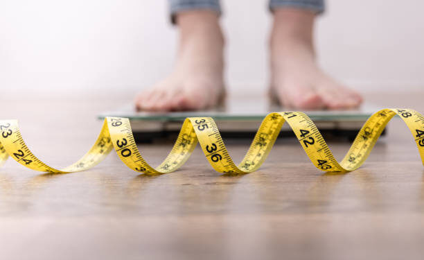 Women's legs on the scales, close-up of a measuring tape, the concept of losing weight, healthy lifestyle.