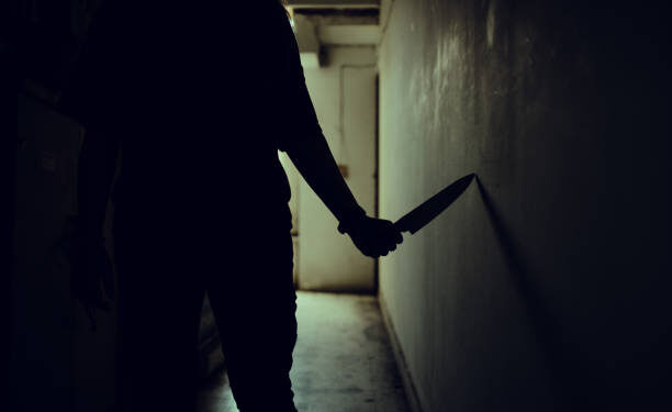 The shadow of a female murderer stood terrifyingly holding a knife and lit from behind.Scary horror or thriller movie mood or nightmare at night Murder or homicide concept.