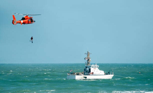 coast guard helicopter lowering diver into the ocean near a coast guard ship