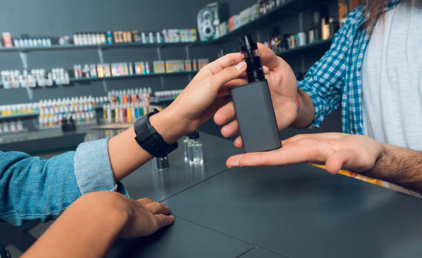 The girl came to the vapeshop. She talks with the seller - a tall man with long hair and a beard. The store has a large selection of electronic cigarettes.