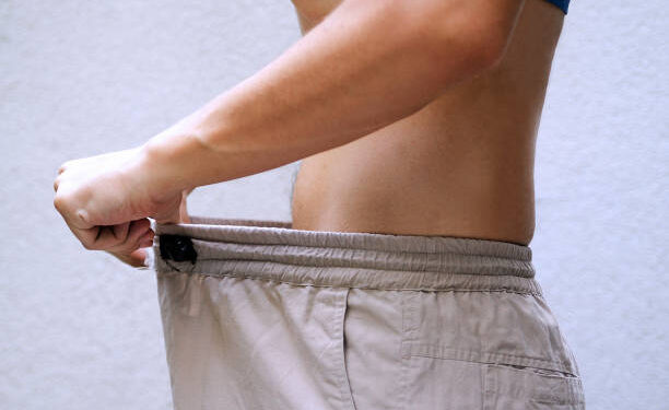 Man after diet comparing his waist size of trousers.Slim fit male body or genital issue.