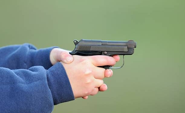Close up photograph of young girl person holding semi automatic handgun pistol.  Image has copy space above and below.