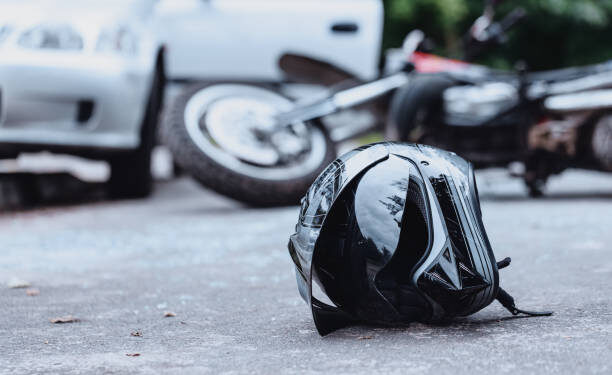 Close-up of a black biker helmet on the street with overturned motorbike in the background. Road collision concept
