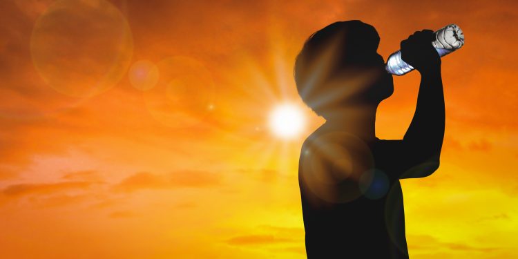 Silhouette man is drinking water bottle on hot weather background with summer season. High temperature and heat wave concept.